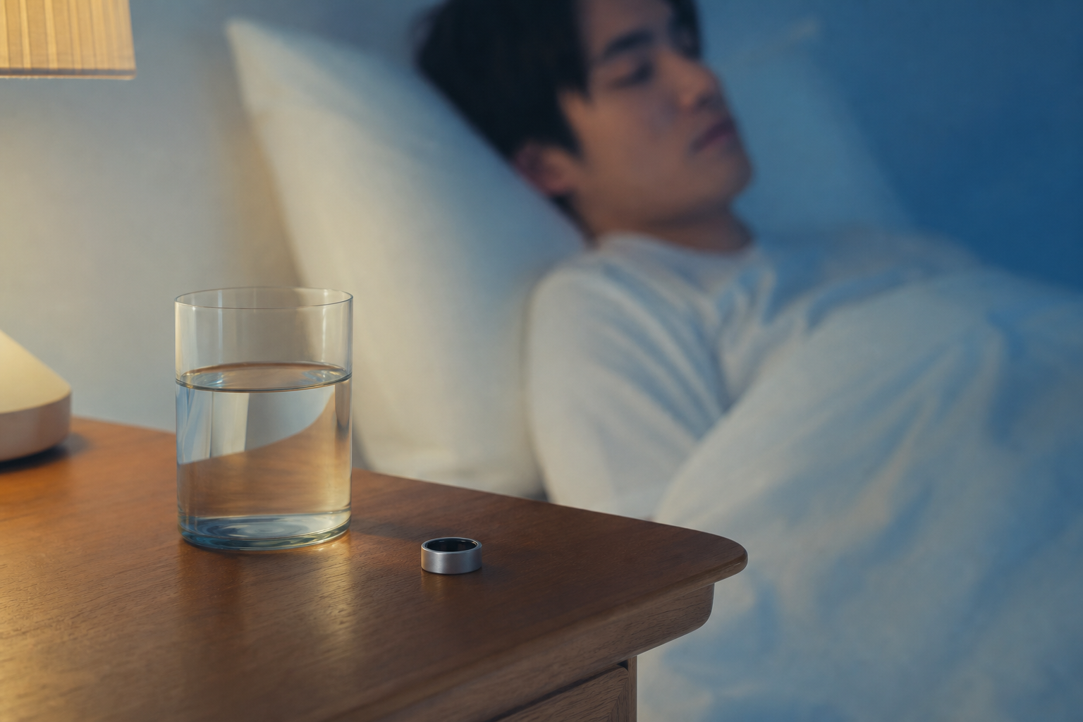 ナイトテーブルに置かれたスマートリングと水のグラス、落ち着いた寝室の夜景