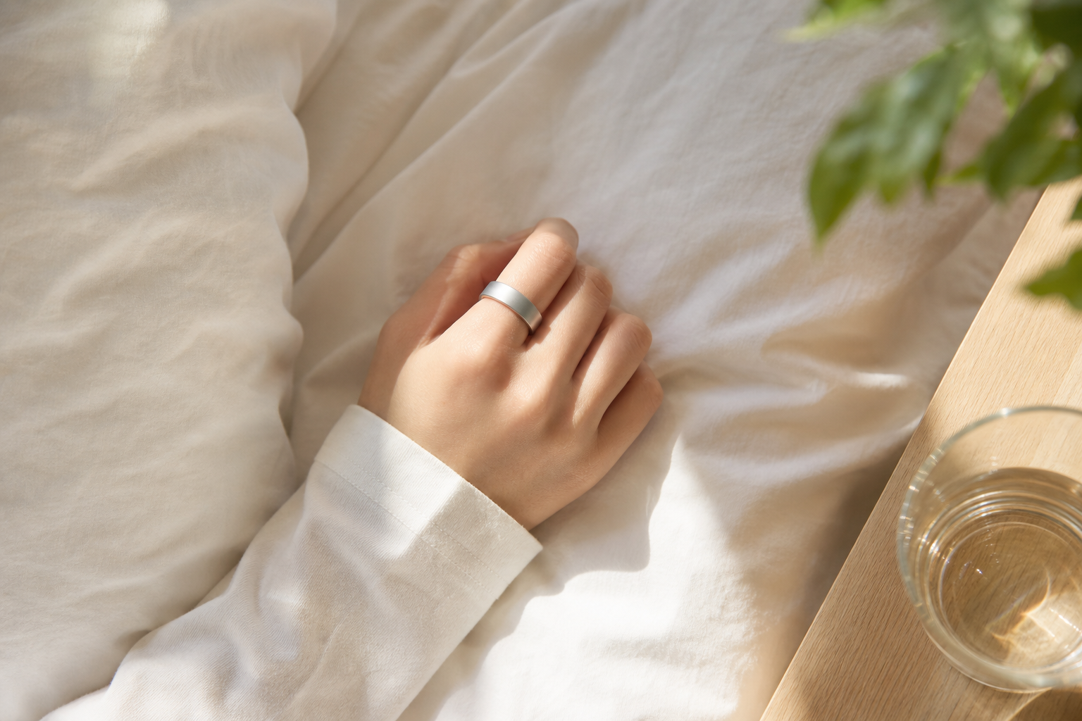 睡眠トラッカーを着けた手元と朝の寝室
